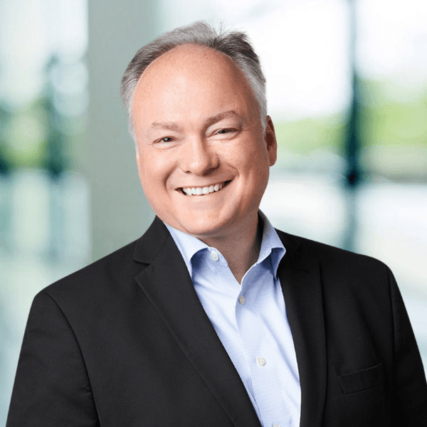 Middle-aged businessman in black suit and blue shirt smiling warmly in a bright, modern office setting