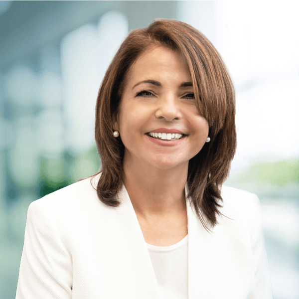 Smiling professional woman with shoulder-length brown hair wearing a white blazer and white top in a bright