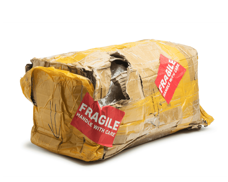 A badly damaged yellow shipping package with red "FRAGILE" labels, torn open with visible internal packaging